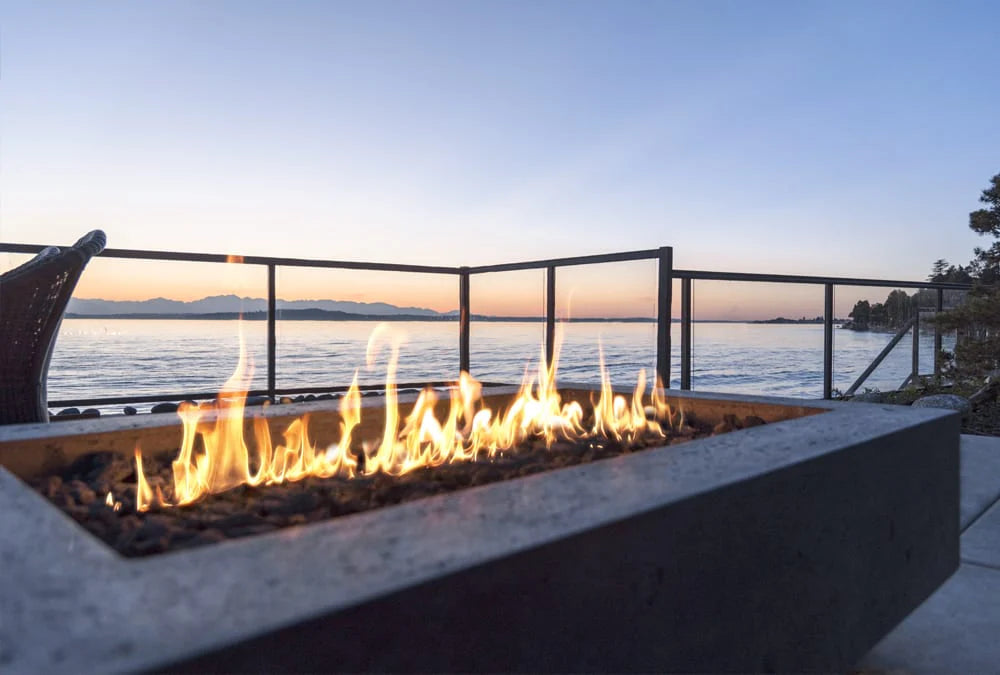 Prism Hardscapes Fire Table lit on patio with beautiful water background